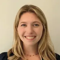The image shows a person with long blonde hair smiling at the camera, wearing a dark top against a neutral background.